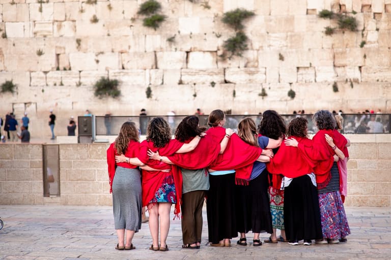 Mothers in matching red shawls standing arm in arm before the Western Wall