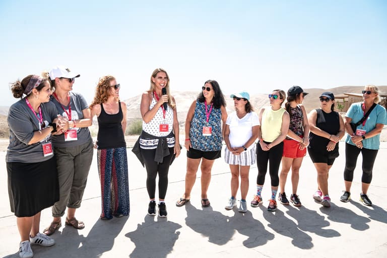 Mothers gathered at a desert lookout while one speaks into a microphone