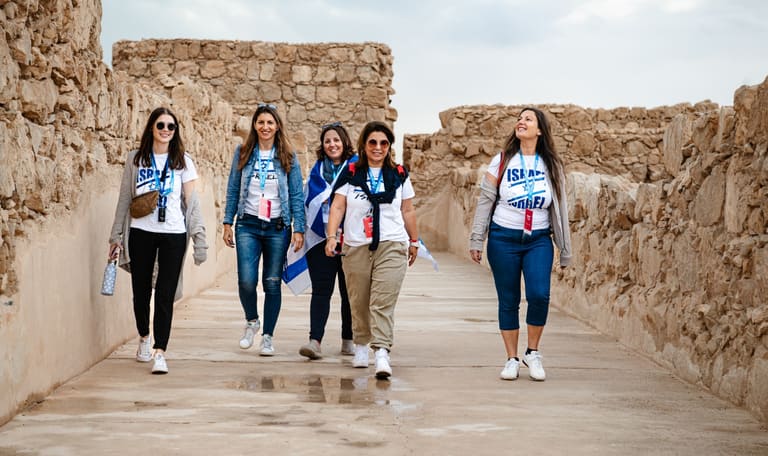 Five mothers in Israel shirts walking a stone corridor at Masada