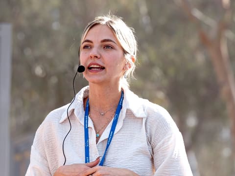 A Momentum educator teaching outdoors under the trees, speaking into a headset microphone