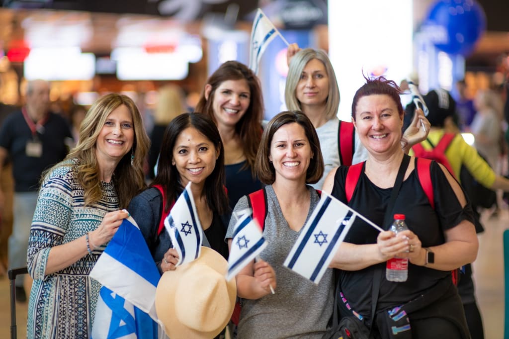 A group of mothers smiling and holding Israeli flags together at the airport